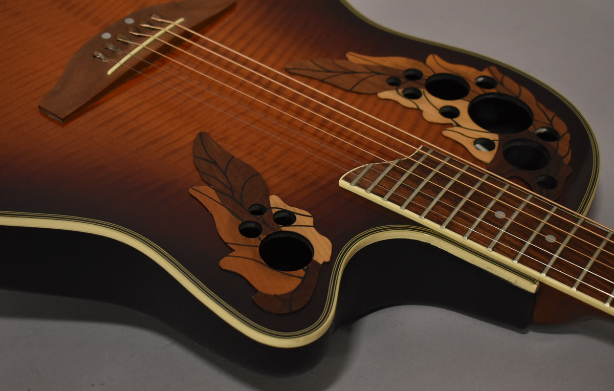 Close-up of the sunburst body and fretboard, showing the ornate leaf-shaped soundholes and the bridge with six strings.