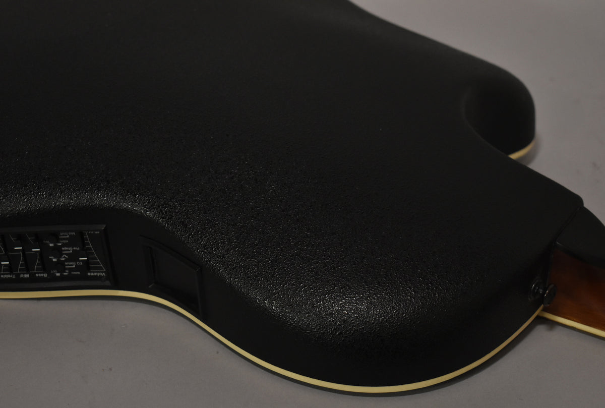The guitar's textured black composite back and side are visible, with a cream binding and an onboard preamp control panel.