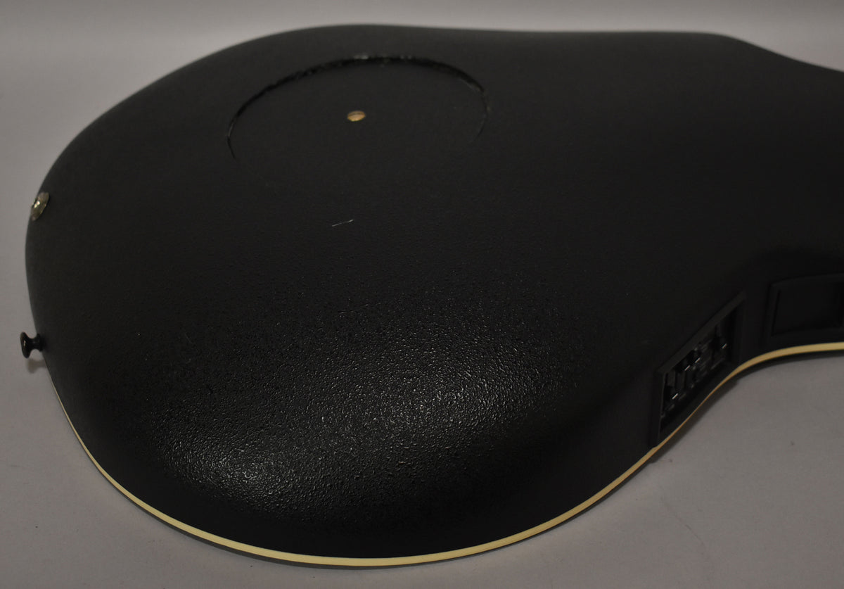 Close-up of the guitar's textured black composite back, showing a circular soundhole, strap button, and side-mounted preamp controls.