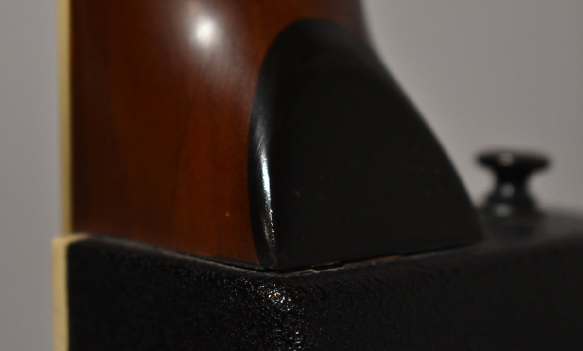 Close-up of the guitar's neck heel, showing the dark brown neck, black heel cap, and a small crack where it meets the body.