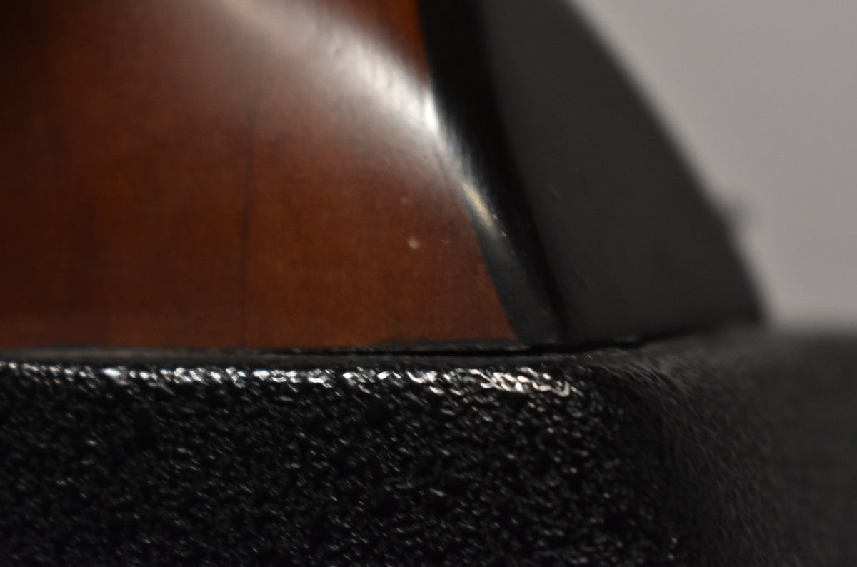 Close-up of the guitar's dark brown body and black binding, showing minor scuffs and a few small white flecks.