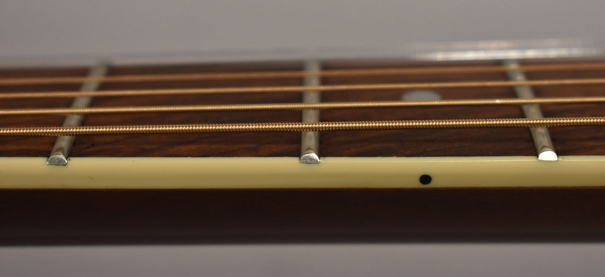 Close-up of the dark fretboard and bronze strings, showing light cream binding with a small black dot inlay.