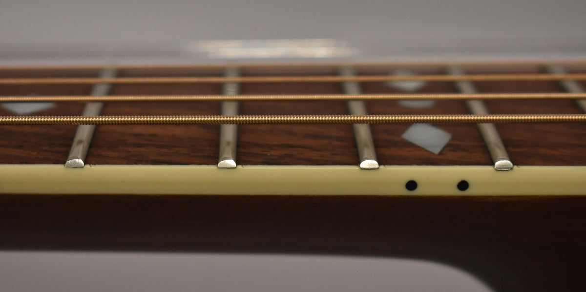Close-up of the dark wood fretboard with diamond inlays, showing the frets, strings, and two black side dot markers.