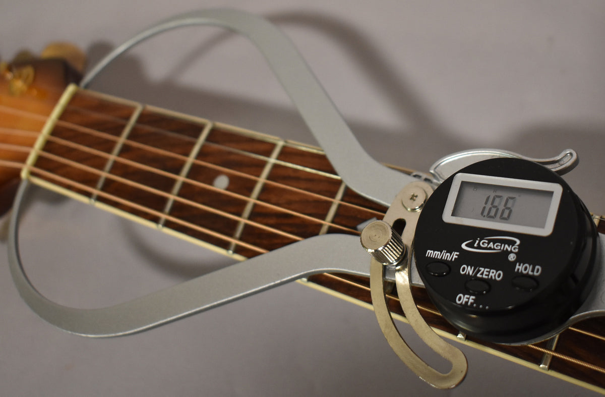 A digital caliper measures the nut width of the guitar's dark wood fretboard, showing 1.66 on its screen.