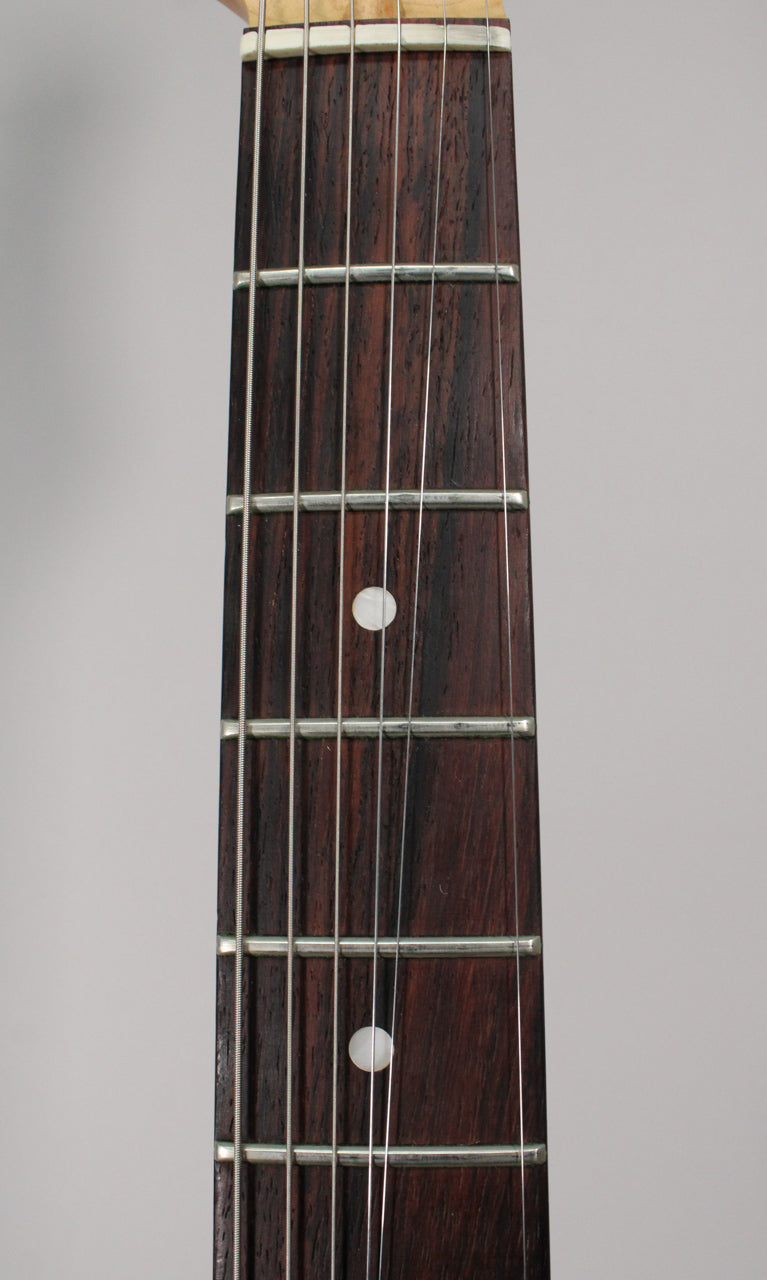 Close-up of the dark rosewood fretboard with white dot inlays, showing the nut and frets 1-7, with light wear.