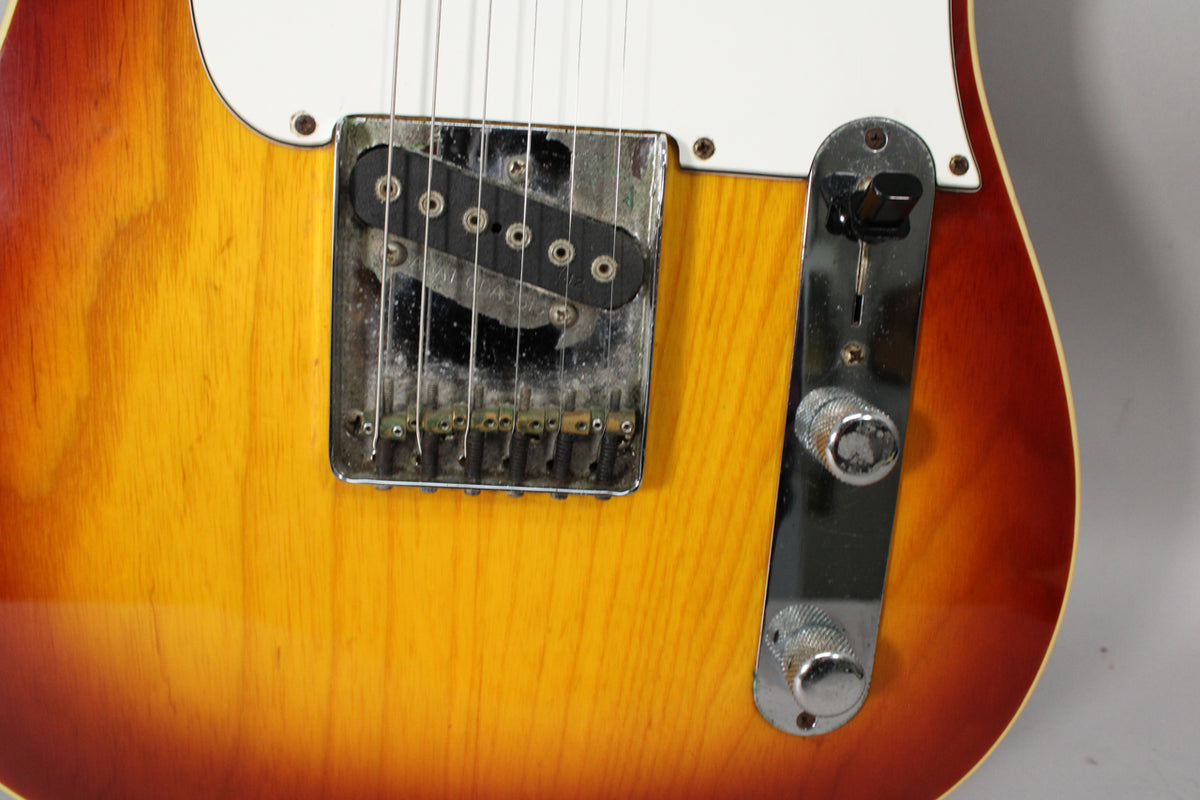 Close-up of the sunburst guitar body, showing the worn chrome bridge with single-coil pickup and the control plate with two knurled knobs.