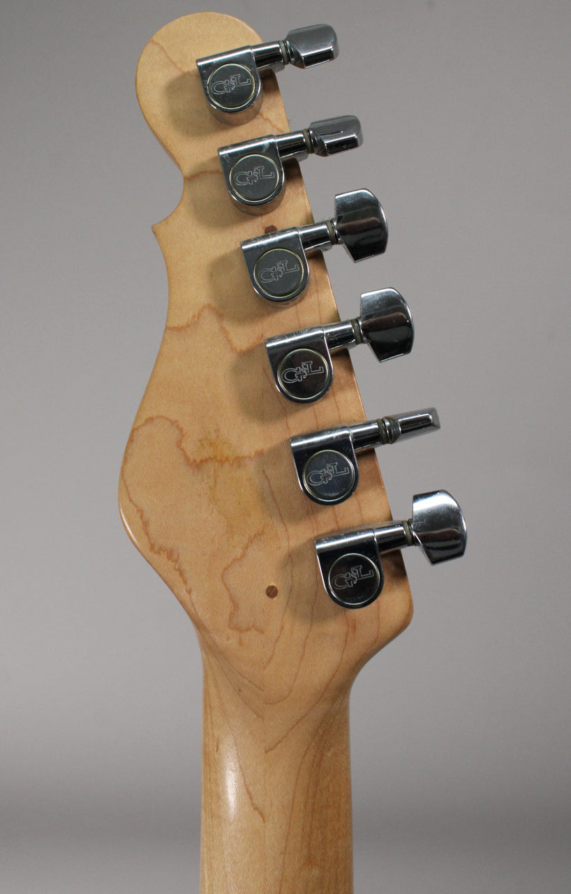 The back of a light wood headstock with six chrome tuners, showing some finish wear and a small ding.