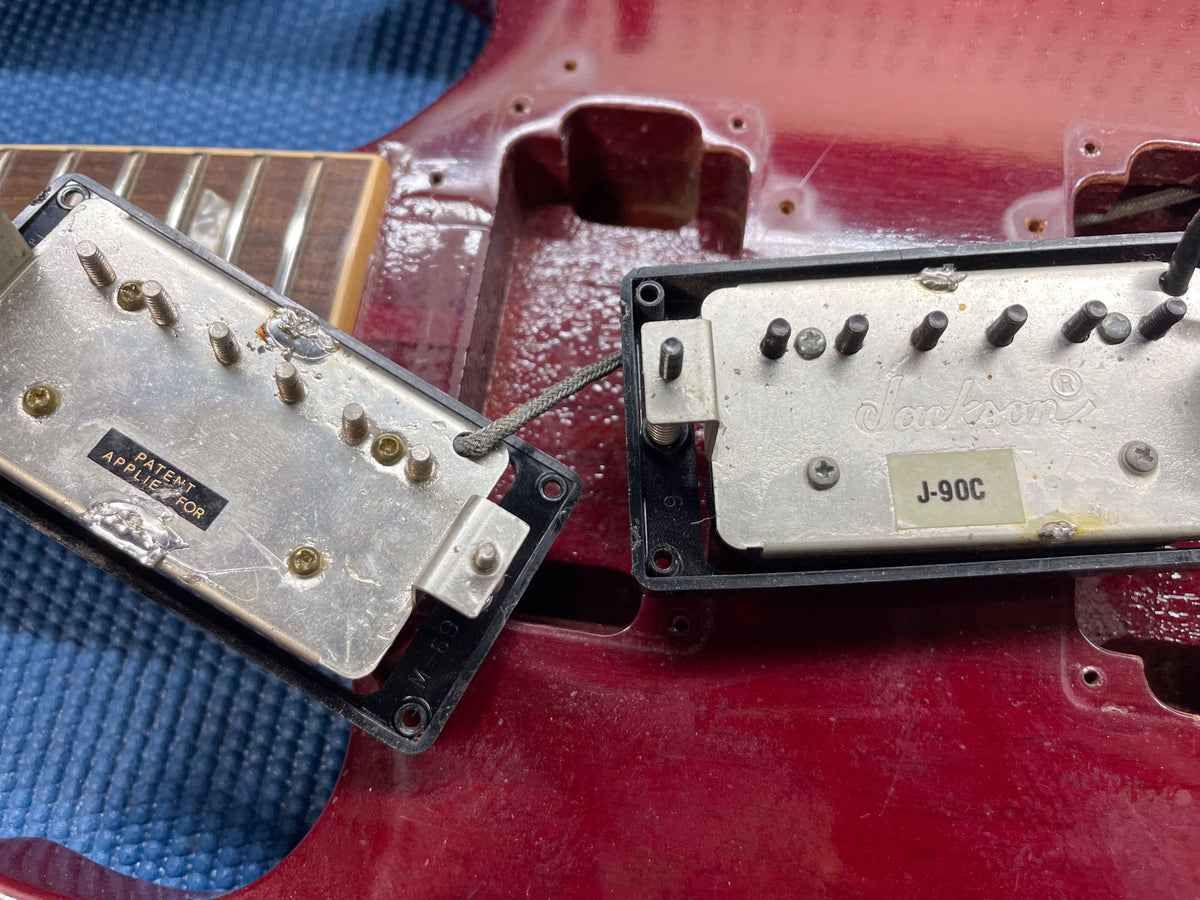 Two guitar pickups, one marked "PATENT APPLIED FOR" and the other "Jackson J-90C", rest on a cherry red guitar body.