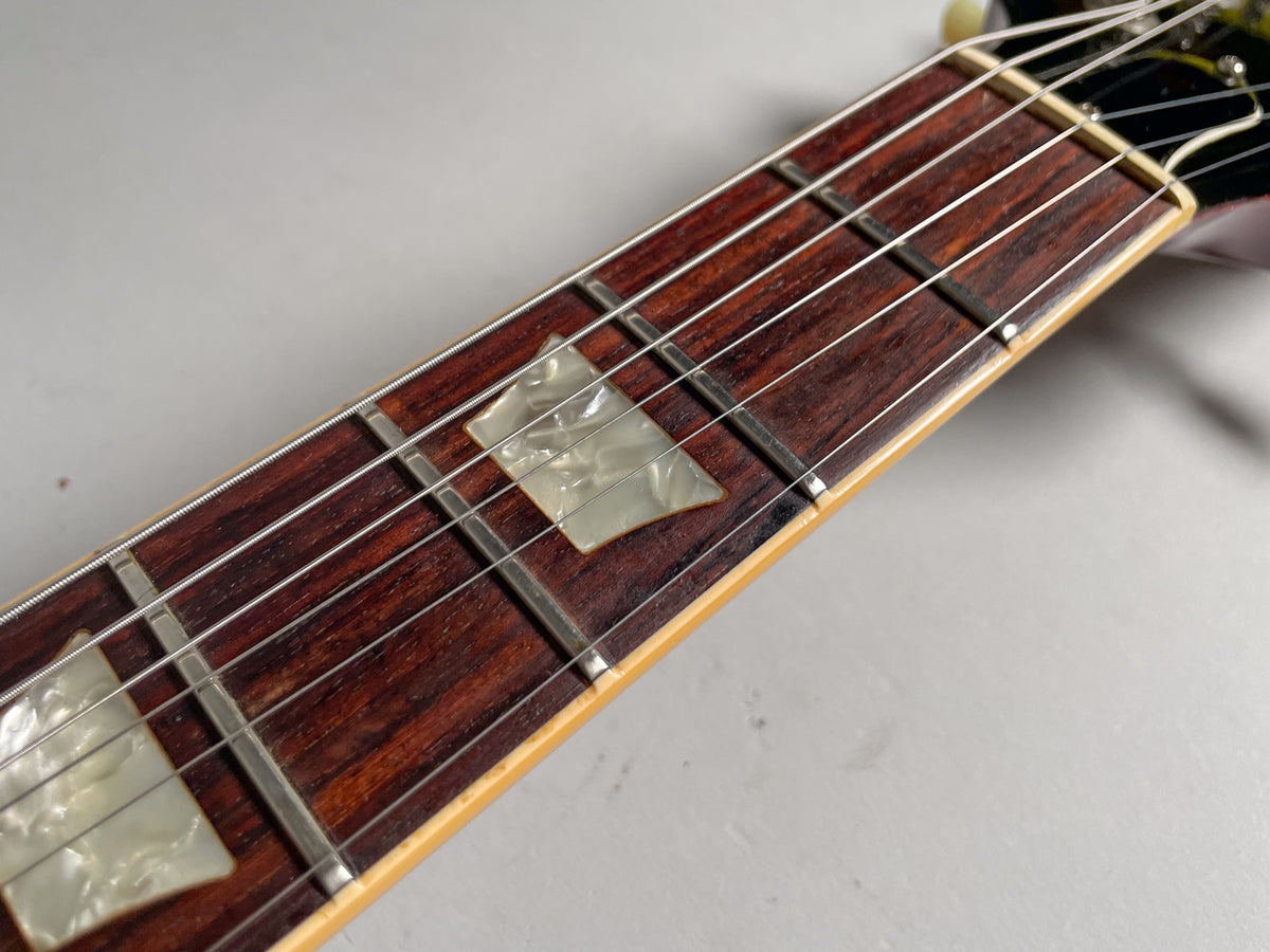 Close-up of the dark rosewood fretboard with trapezoid mother-of-pearl inlays, showing some wear and string marks.