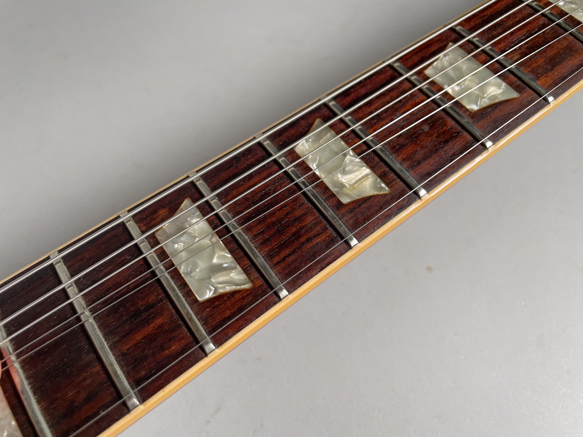 Close-up of the dark rosewood fretboard with trapezoid pearloid inlays and silver frets, showing light wear on the wood.