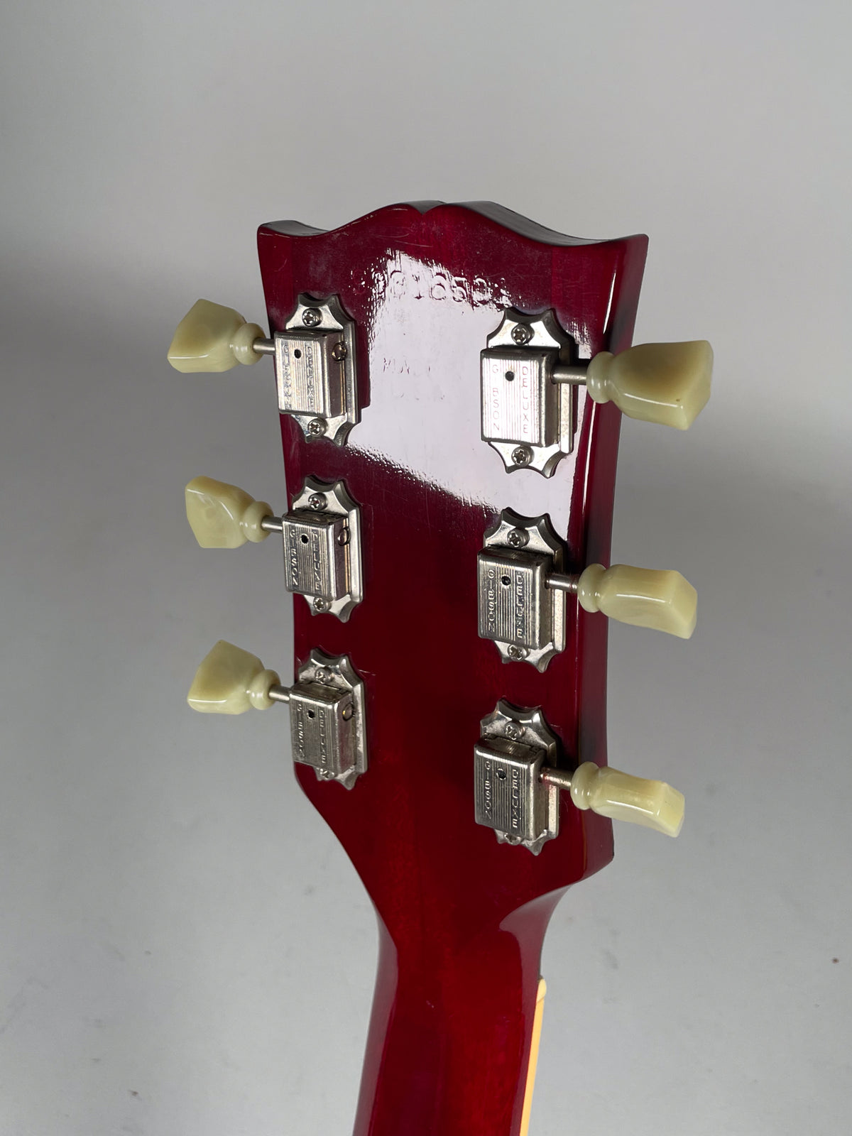 Rear view of the cherry red headstock and neck, showing six cream-colored tuning pegs and chrome tuners with light wear.