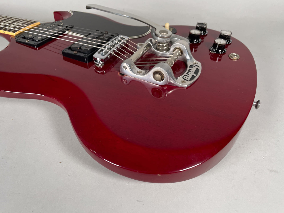 Cherry red SG body, angled from the lower bout, showing a Bigsby vibrato, black pickguard, and four black control knobs.
