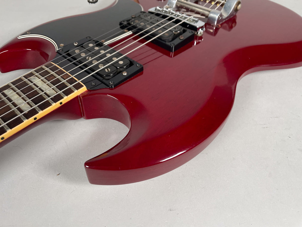Close-up of the cherry SG body, showing the black pickguard, humbucker pickups, and Bigsby vibrato system.