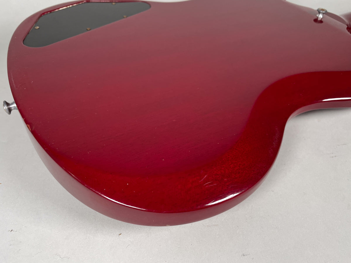 The back of a cherry red SG, showing a black control cavity cover, strap button, and light scratches on the lower bout.