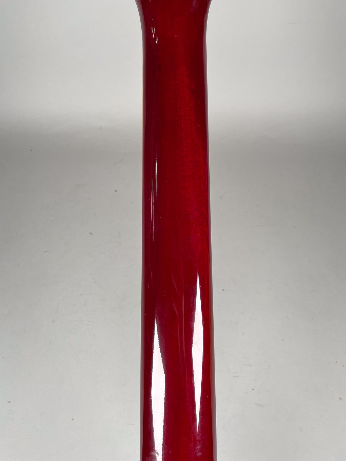 The guitar's cherry red neck, with a glossy finish and visible light wear, is shown vertically against a white background.