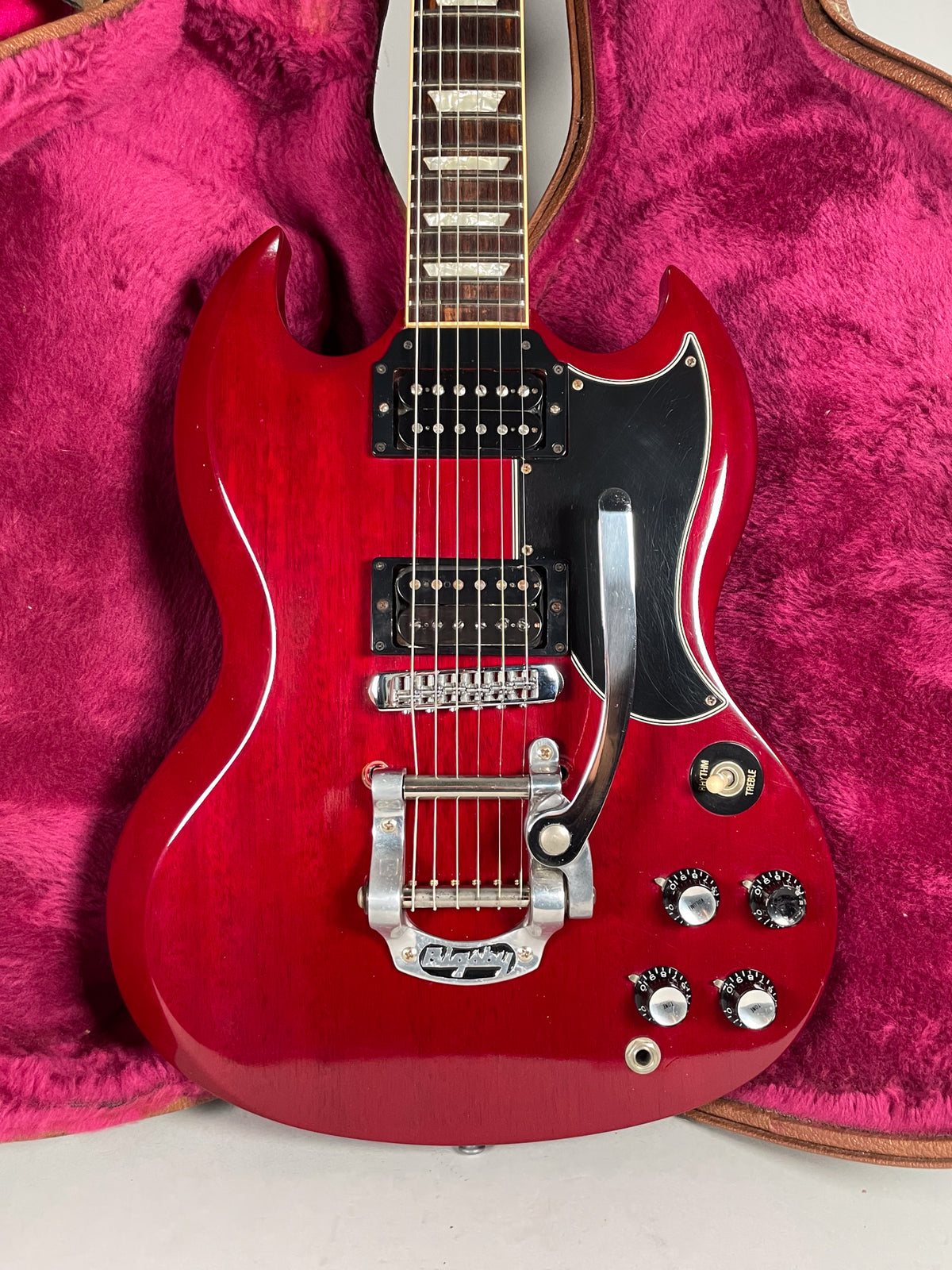 Full-frame shot of a cherry red SG with a Bigsby vibrato, black pickguard, and four black control knobs.