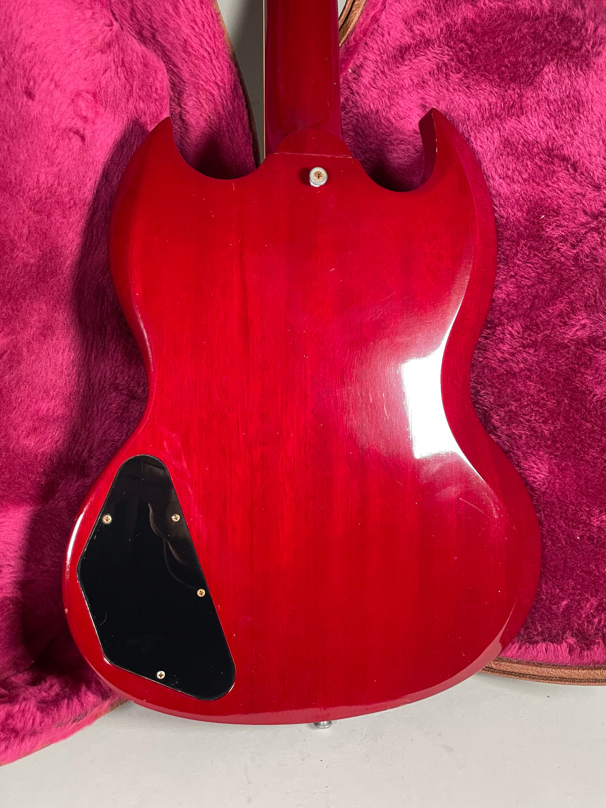 The back of a cherry red SG, showing the neck joint, black control cavity cover, and light surface wear.