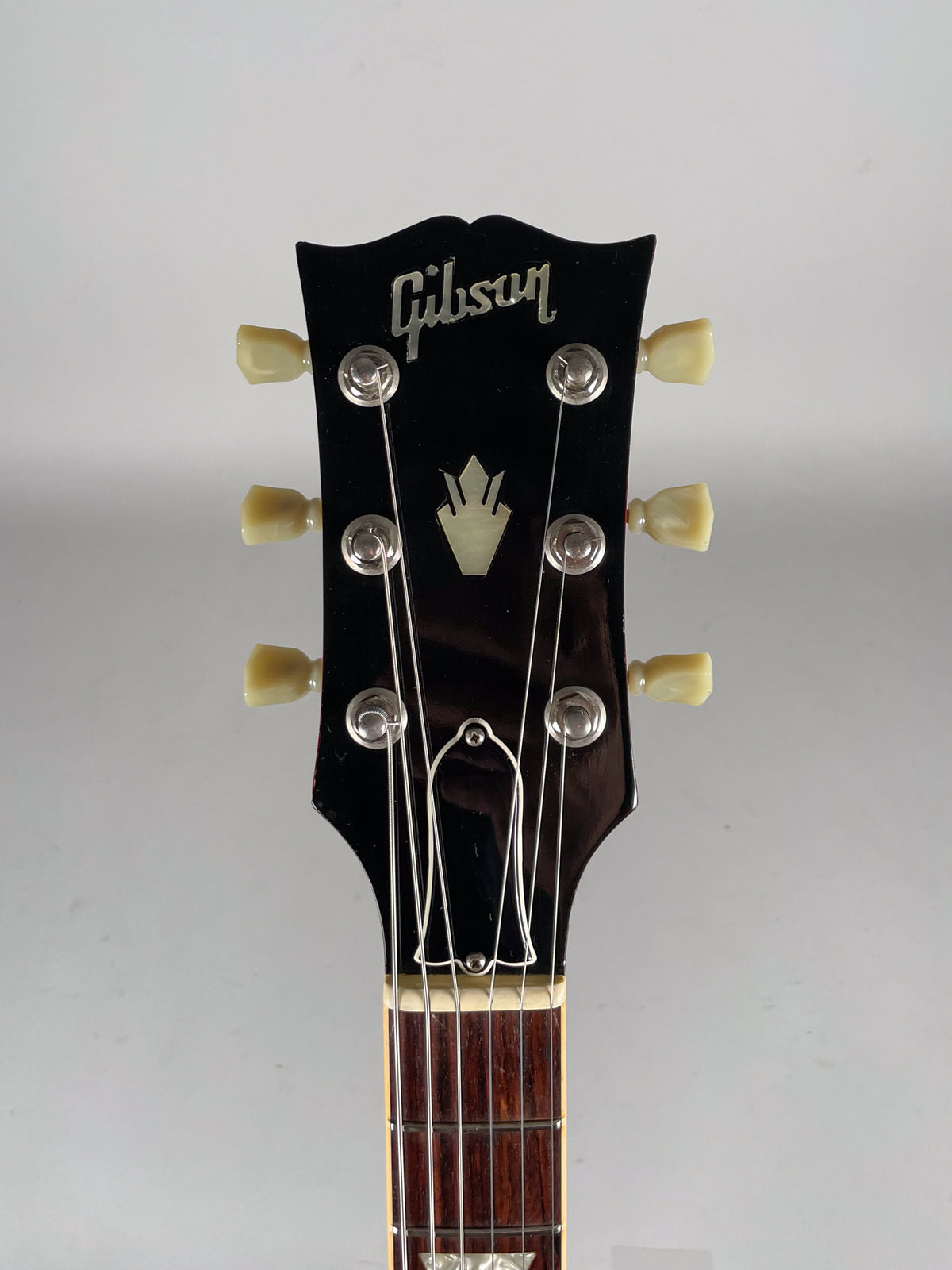 The guitar's glossy black headstock with cream tuning pegs and an inlaid crown is centered, showing the top of the fretboard.