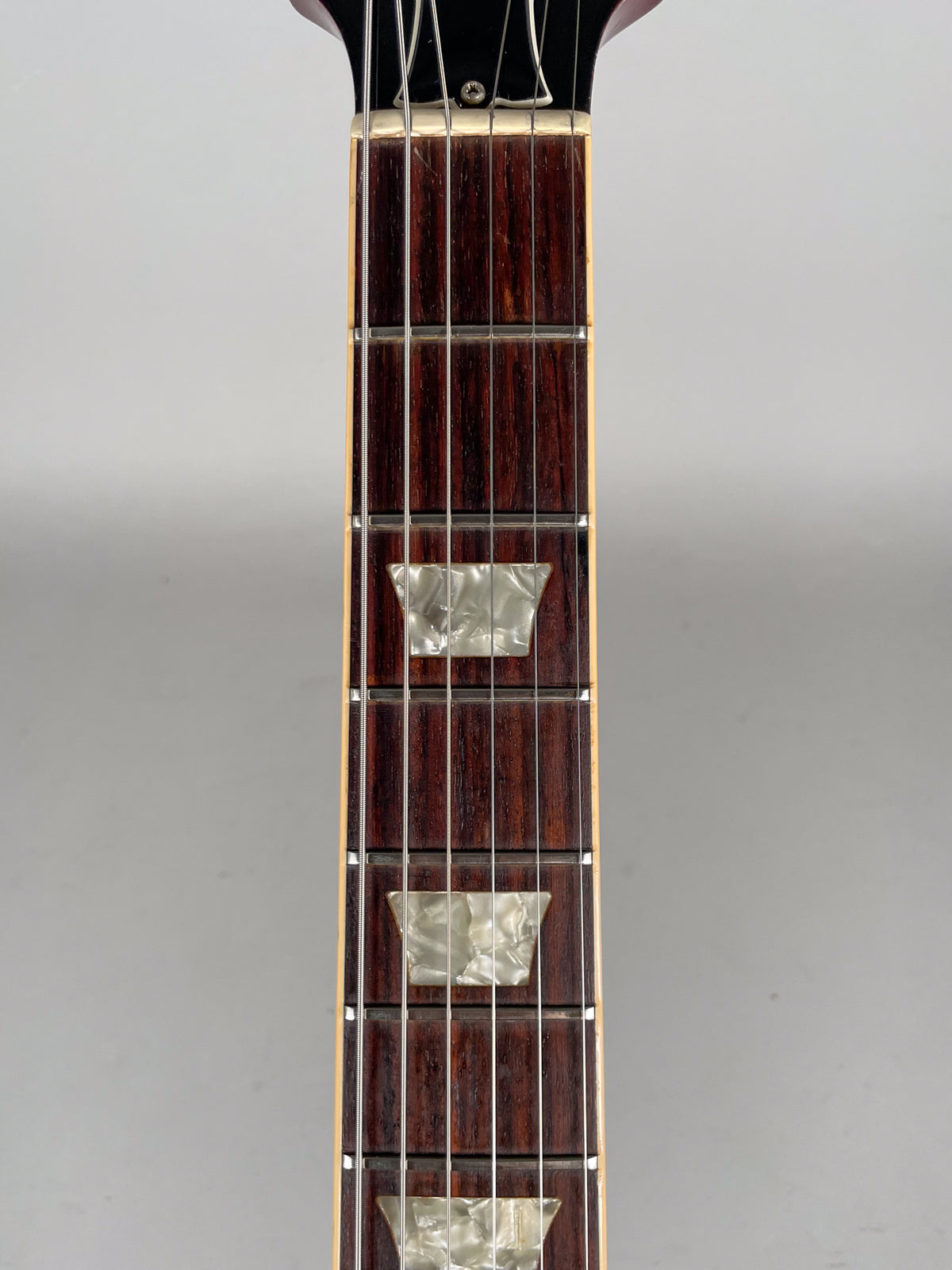 Close-up of the dark rosewood fretboard with trapezoid mother-of-pearl inlays, showing light wear on the frets and strings.
