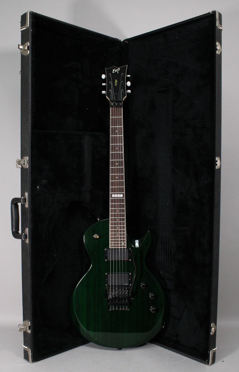 Full view of a dark green electric guitar with a Floyd Rose tremolo system, black hardware, and two humbucker pickups, standing in its open hard case.