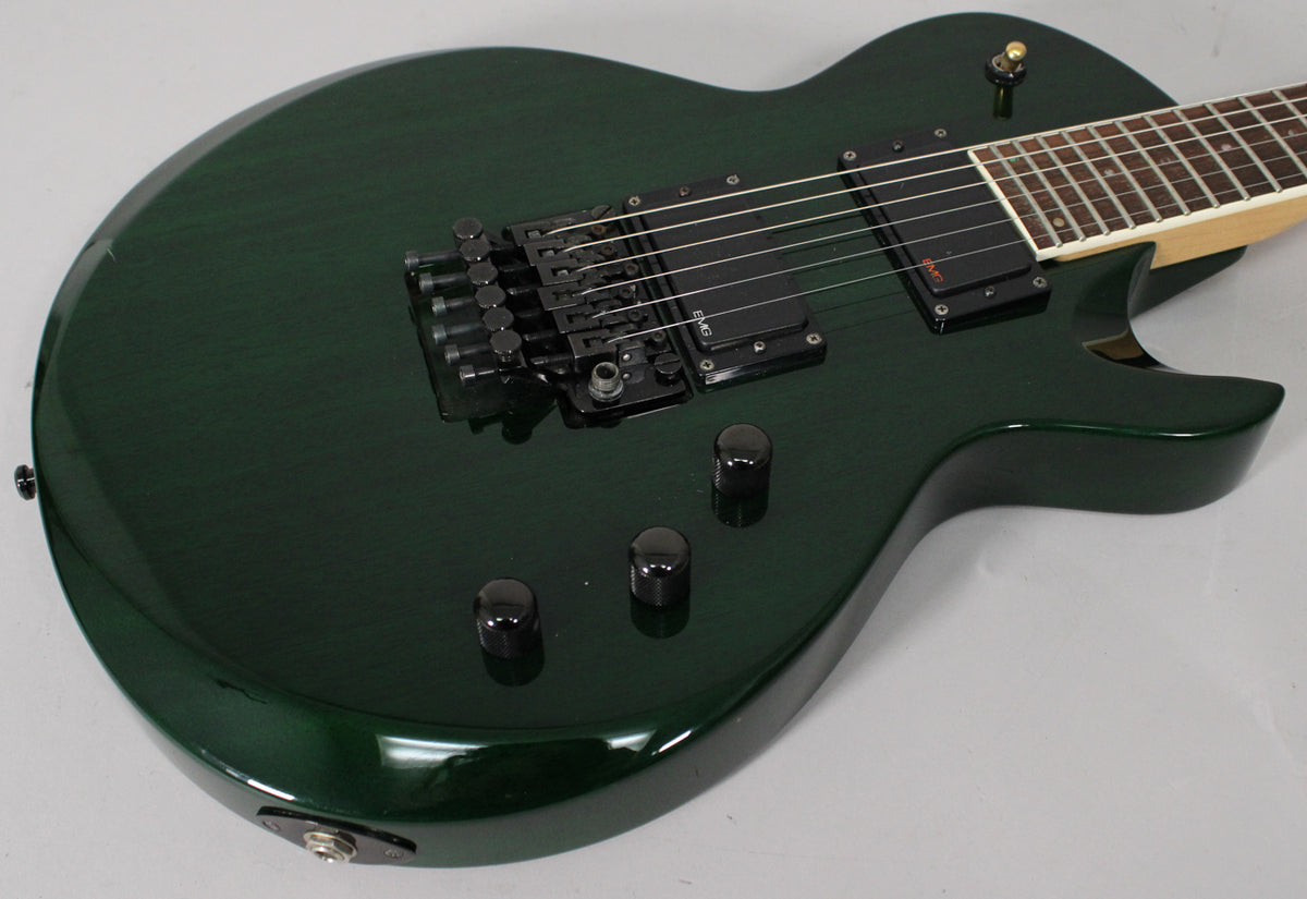 Dark green electric guitar, angled from the lower bout, showing black Floyd Rose tremolo, two humbuckers, and three control knobs.