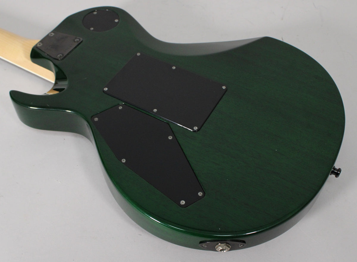 The back of a dark green electric guitar, showing the neck joint, control cavity covers, and output jack.