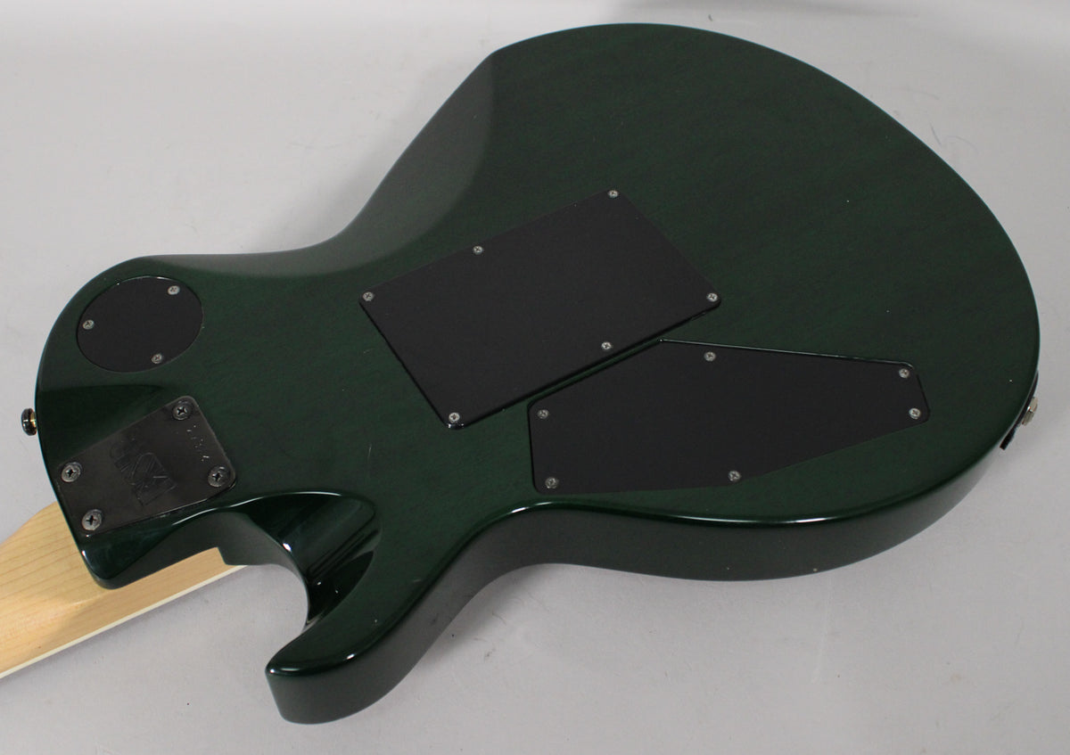 The back of a dark green electric guitar with a maple neck, showing three black control cavity covers.