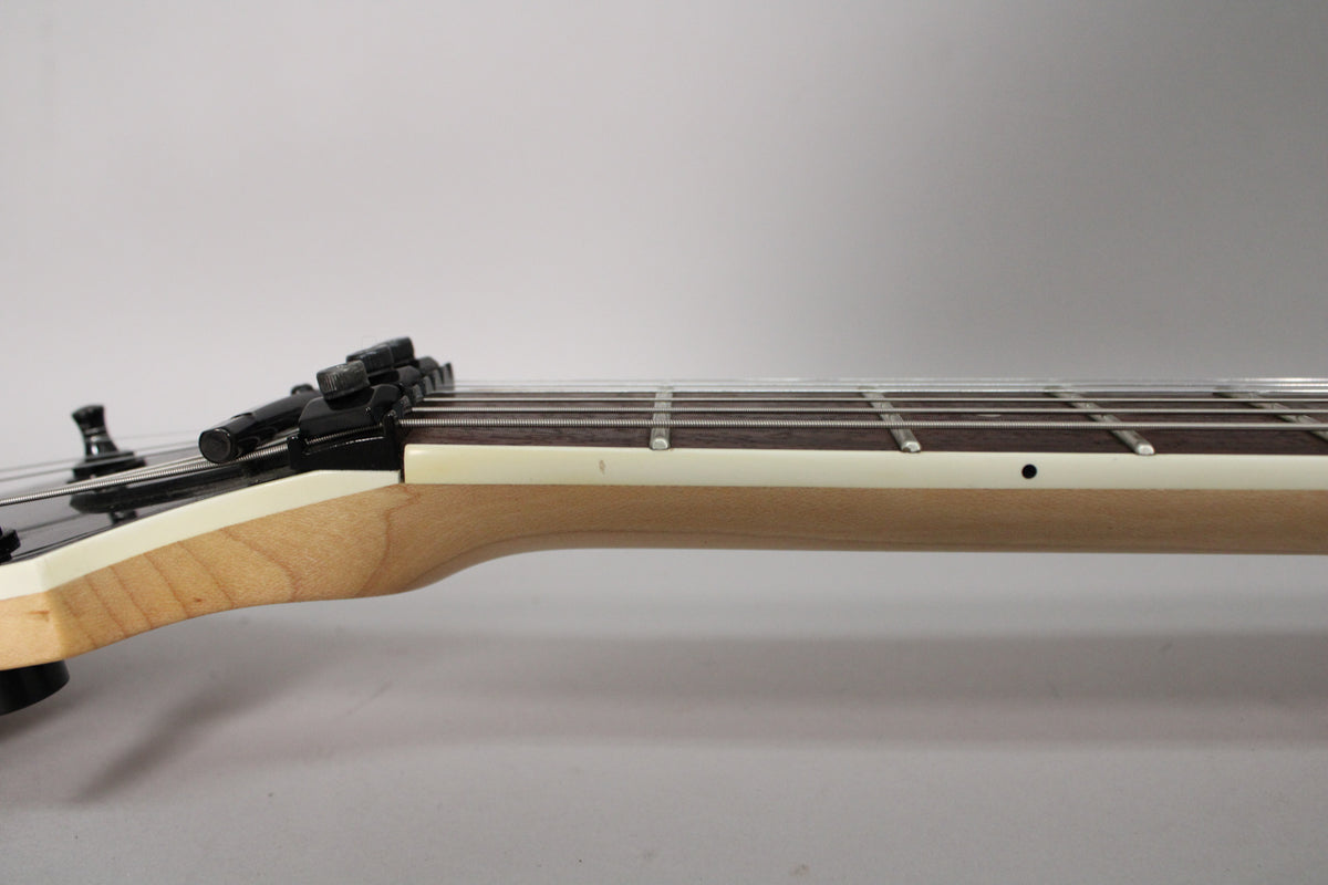 The guitar's light wood neck and dark fretboard are visible from the side, with a black Floyd Rose nut and some wear on the frets.