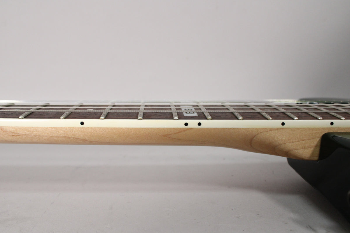 Side view of the guitar neck, showing the light wood finish, dark fretboard with rectangular inlays, and white binding.