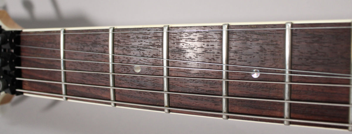 Close-up of the dark brown fretboard with six strings, silver frets, and two circular white fret markers.