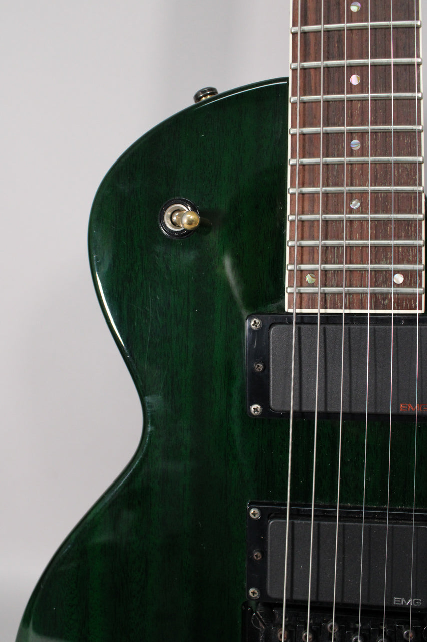 Close-up of the dark green guitar body with wood grain, showing the lower horn, two black humbuckers, and part of the fretboard.