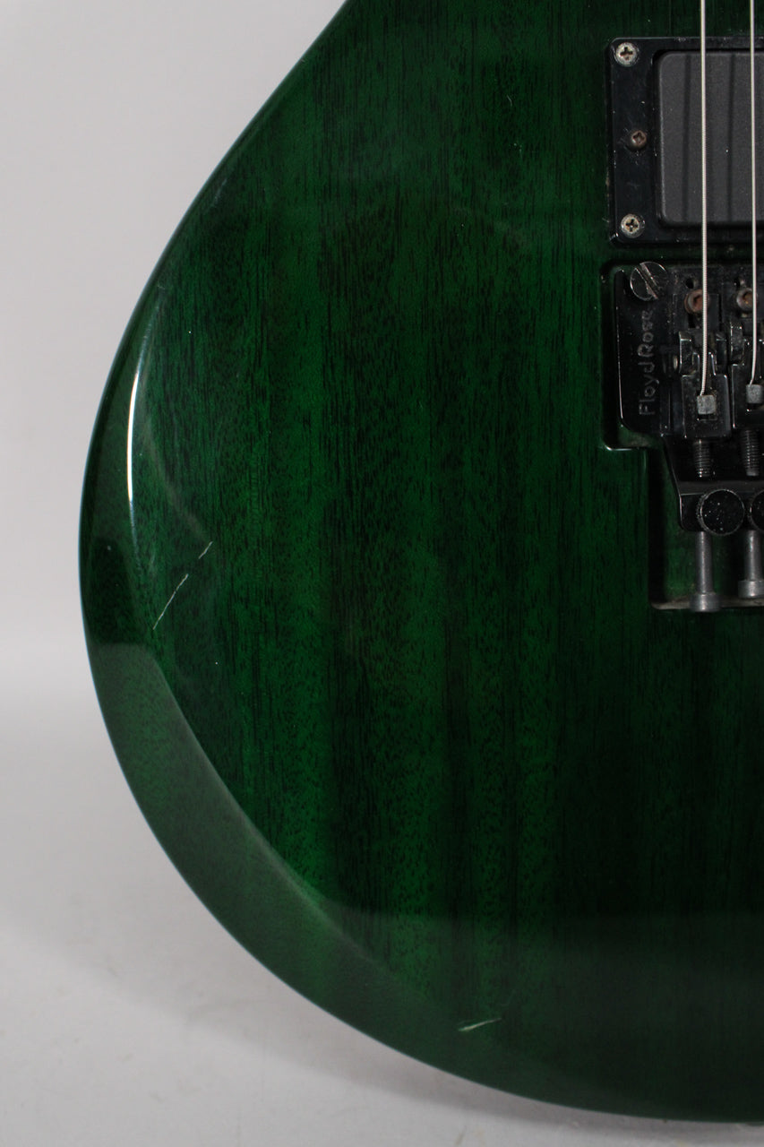 Close-up of the guitar's lower body, showing the dark green finish with wood grain, a black Floyd Rose tremolo, and a scratch on the lower bout.