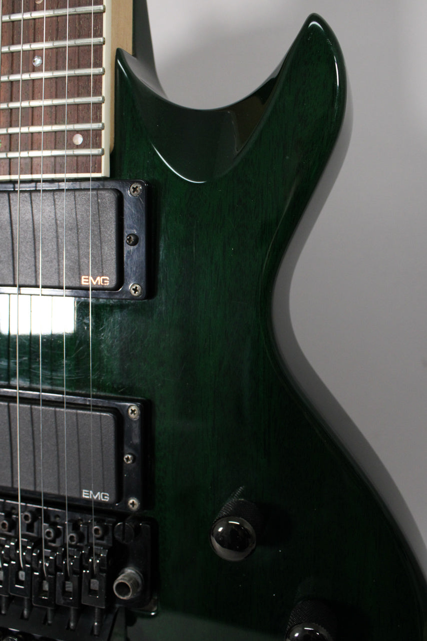 Close-up of the upper body of a dark green electric guitar, showing two black EMG pickups, a Floyd Rose bridge, and a volume knob.