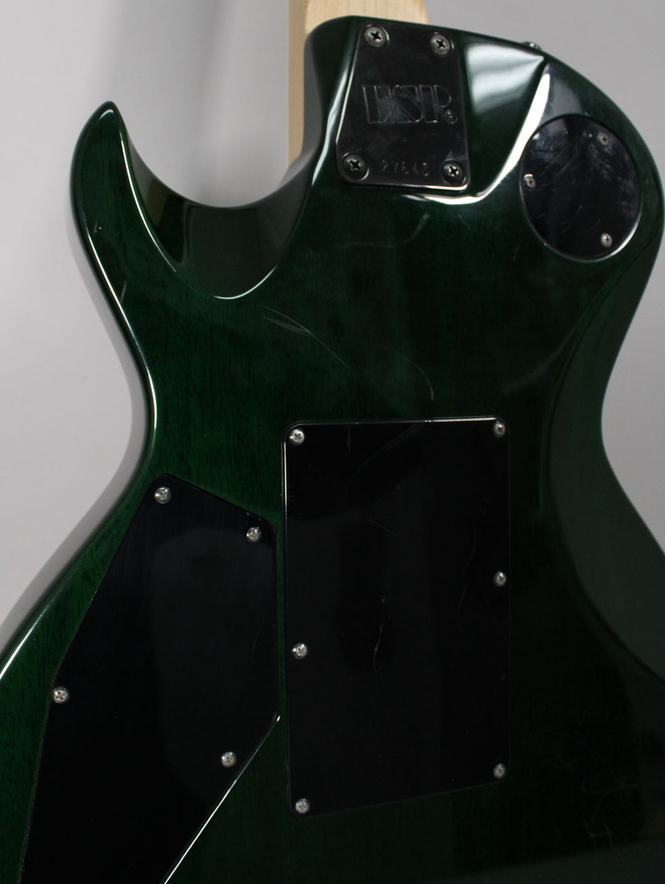 The back of a dark green electric guitar, showing the neck joint, black control cavity covers, and light surface scratches.