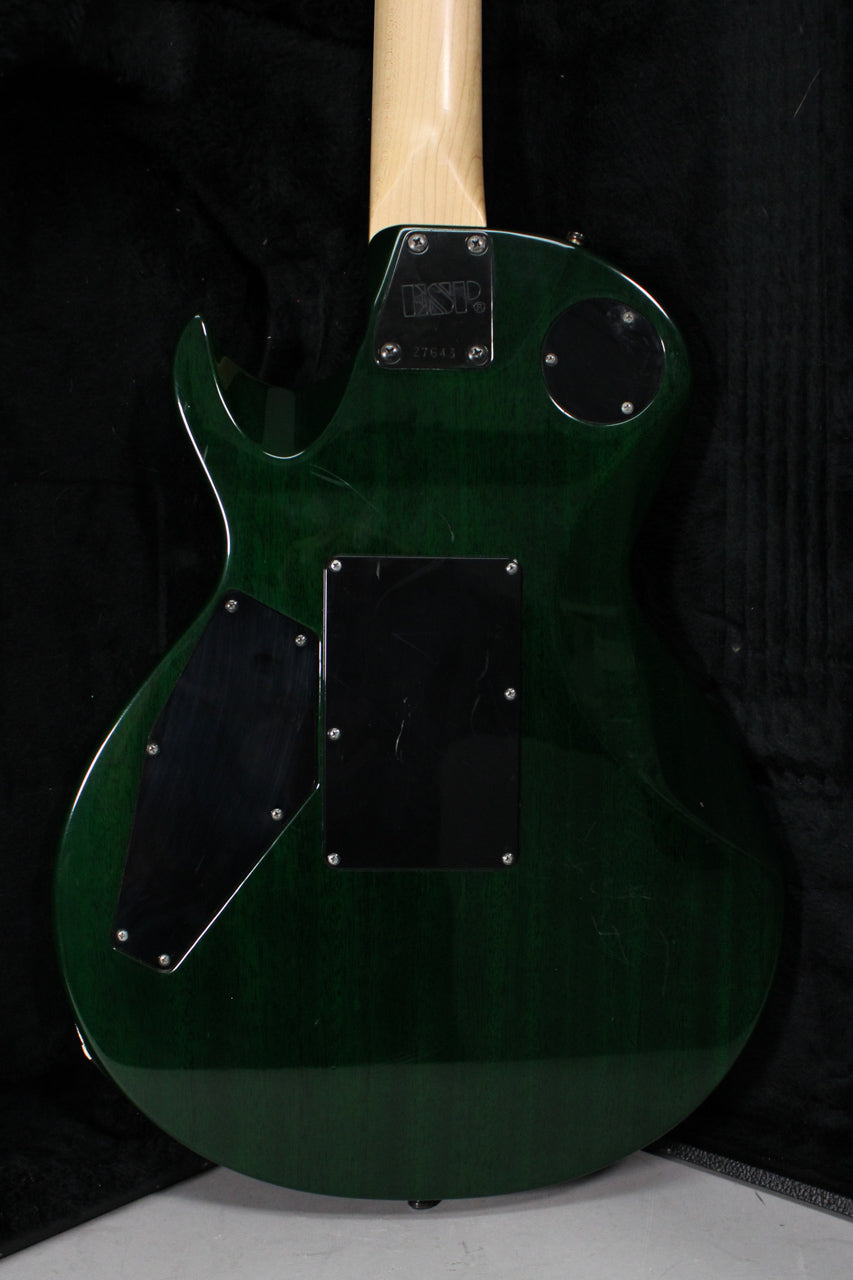 The back of a dark green electric guitar with a natural wood neck, three black control plates, and light surface scratches.