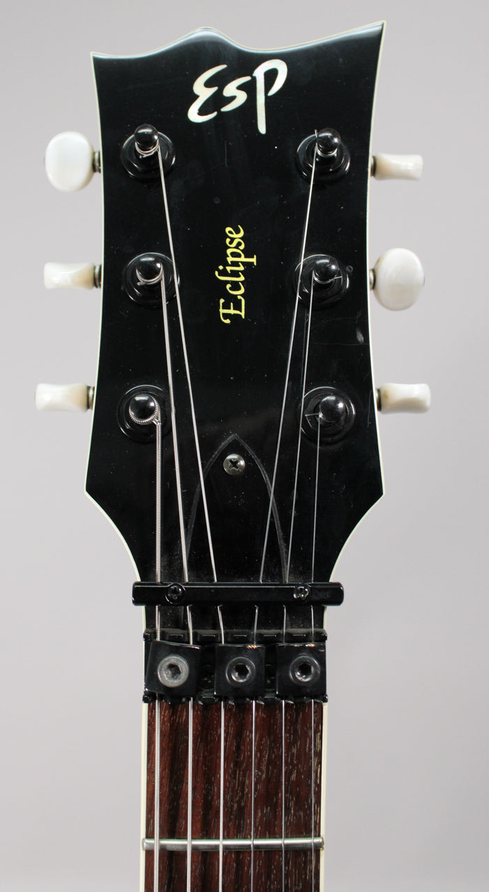 Close-up of the black headstock with white tuning pegs, showing the locking nut and dark rosewood fretboard.