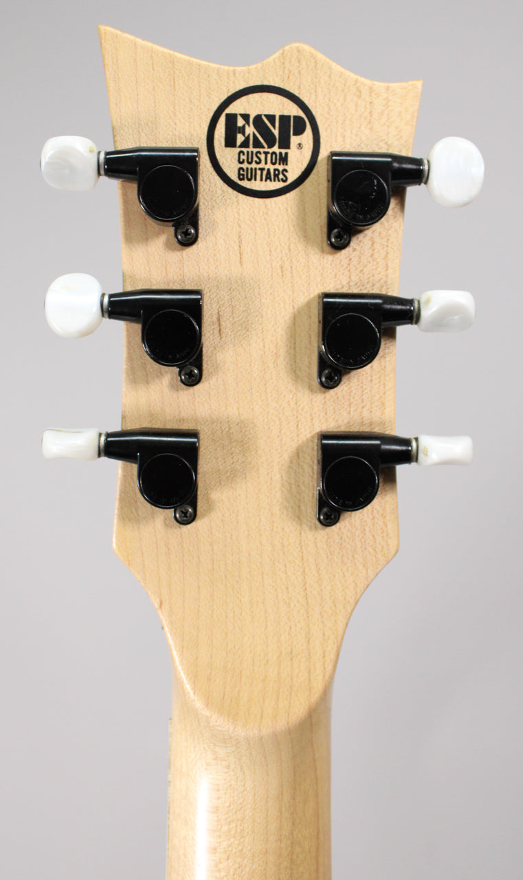 Rear view of the guitar's natural wood headstock and neck joint, showing six black tuners with white pearloid buttons.