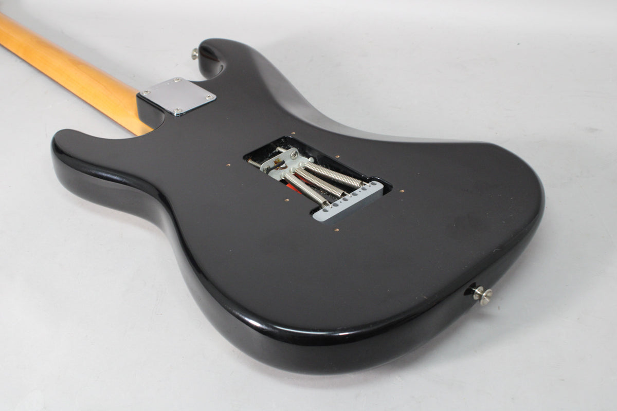 The guitar's black body is viewed from the back, showing the tremolo spring cavity, a chrome neck plate, and a light-colored neck.