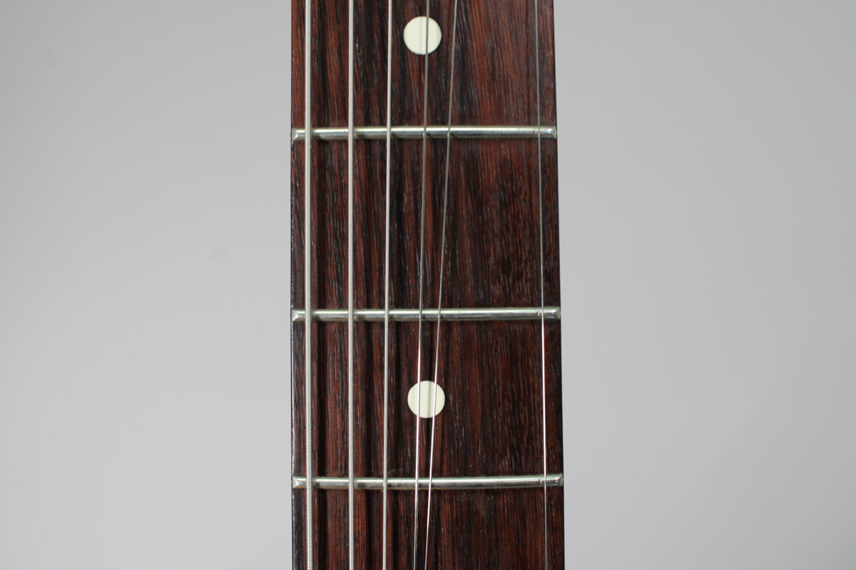 Close-up of the dark rosewood fretboard with white dot inlays and silver frets, showing light wear on the wood.