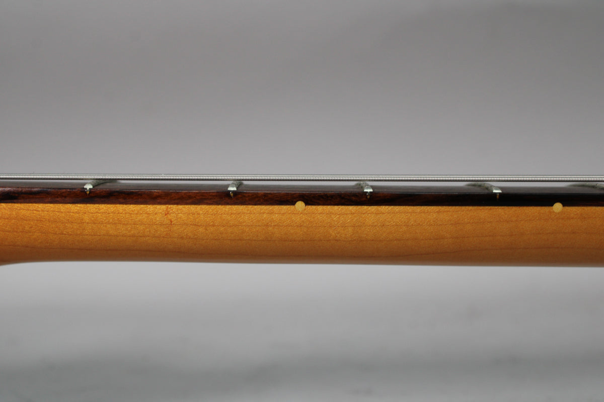 The guitar's light brown neck and dark fretboard are viewed from the side, showing three fret markers and strings.
