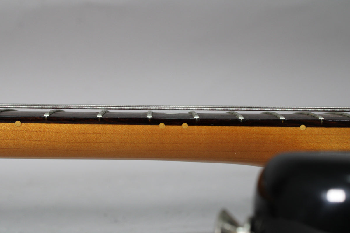 A close-up of the guitar's neck, showing the light brown wood, dark fretboard, and small circular fret markers.
