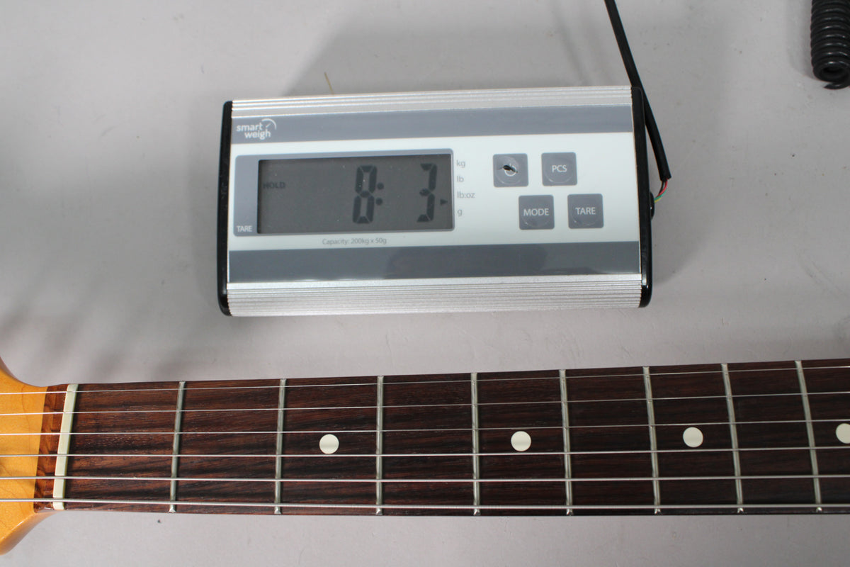 A digital scale displays "8.3-" above the dark rosewood fretboard with white dot inlays and light maple neck.