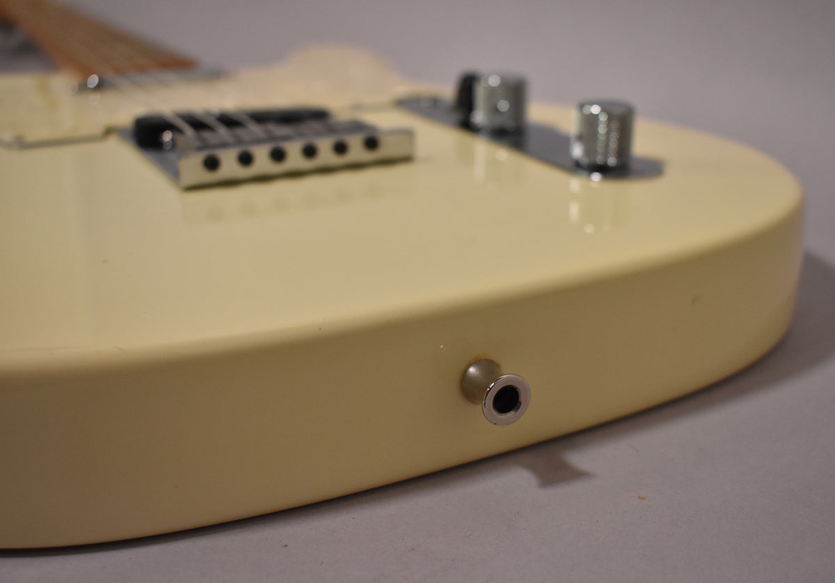Close-up of the Olympic White Telecaster's lower bout, showing the output jack, chrome bridge, and two knurled control knobs.