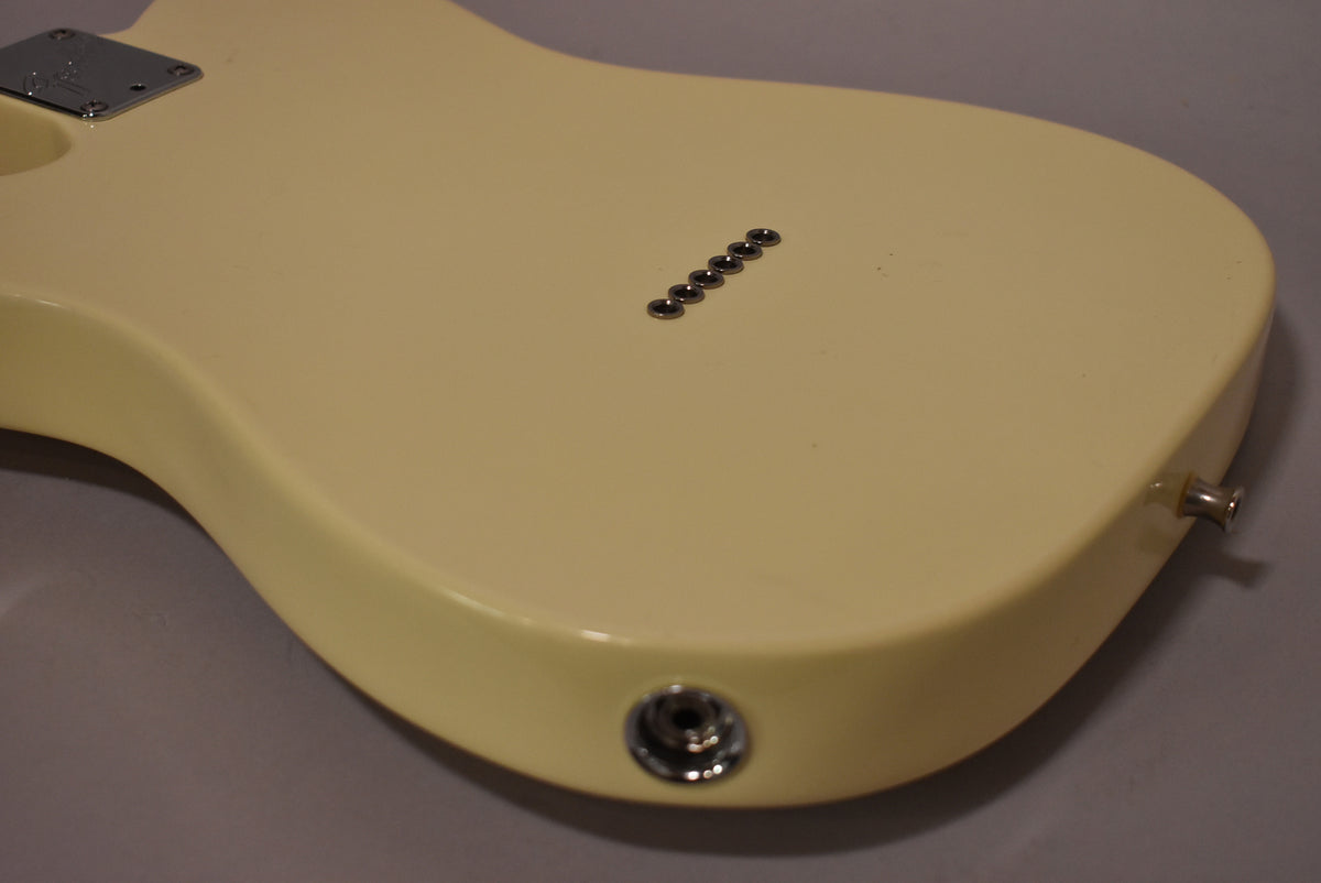 The Olympic White guitar body is shown from the back, revealing six string-through-body ferrules and a chrome output jack on the lower bout.