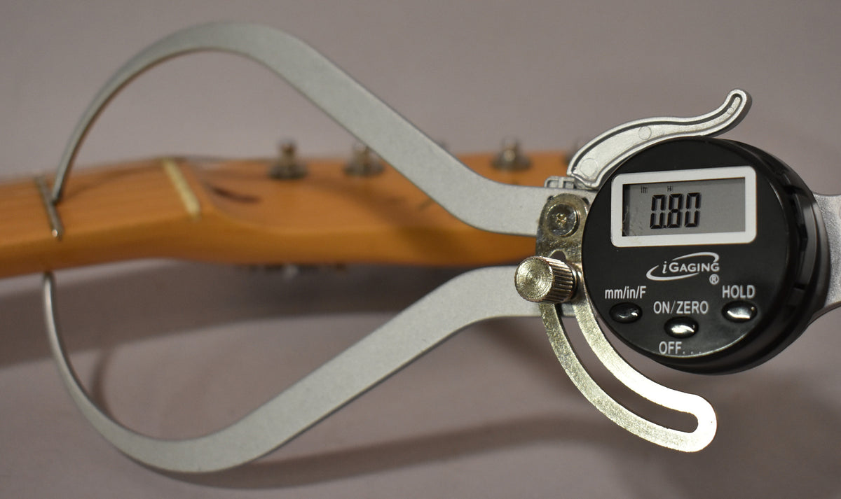 A digital caliper measures the neck relief of a light-colored maple neck, showing "0.00" on its display.