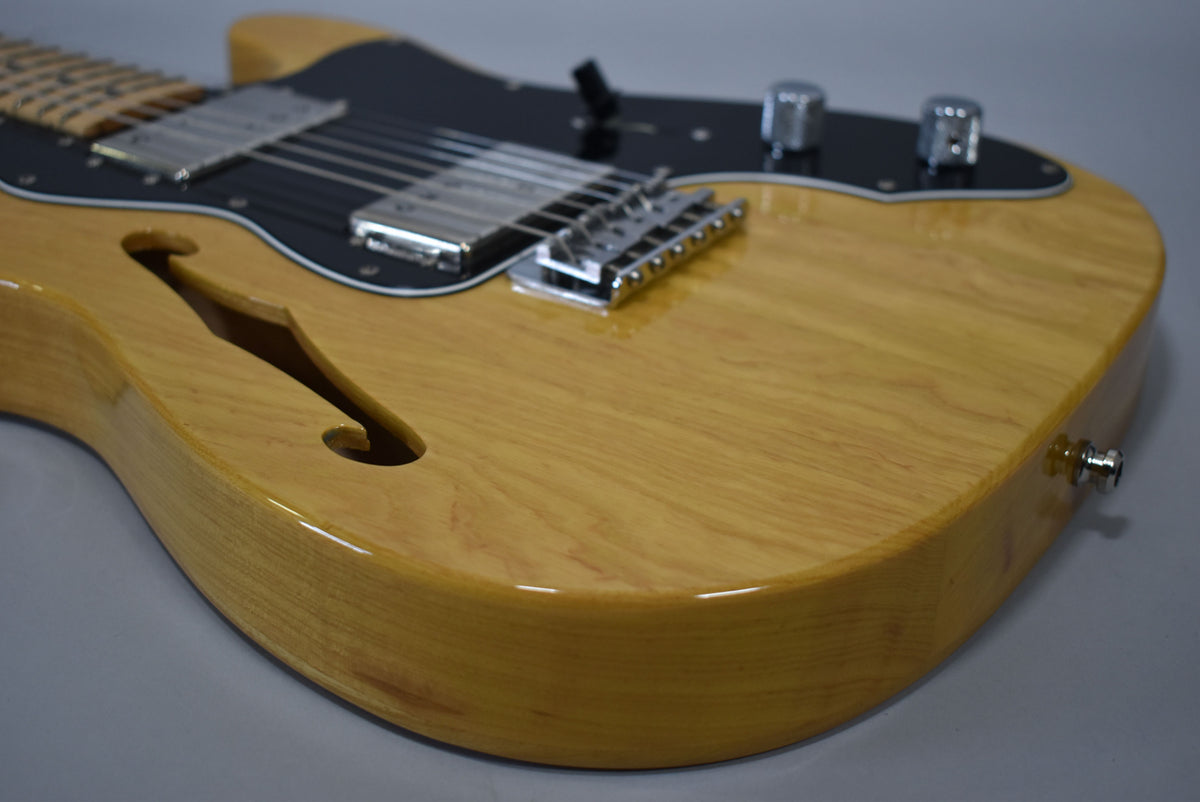 The lower body of a natural finish Telecaster Thinline, showing the f-hole, black pickguard, two humbuckers, and chrome hardware.