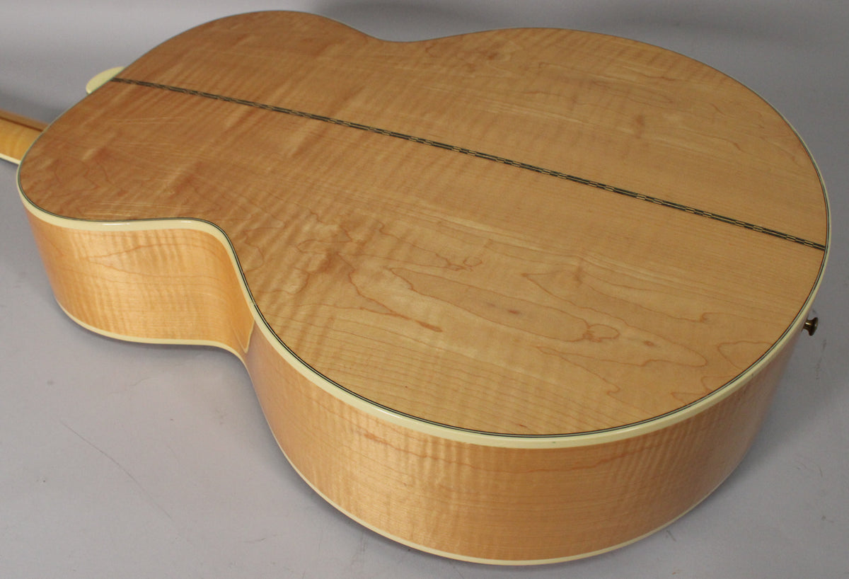 The back of the natural finish acoustic guitar, showing the light wood grain, a dark center seam, and cream binding around the edges.