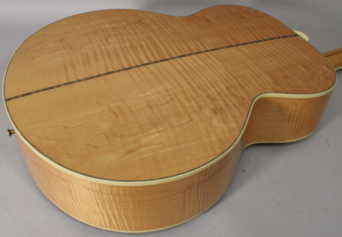 The back of the natural finish acoustic guitar shows a flamed maple grain, with a dark center strip and cream binding.