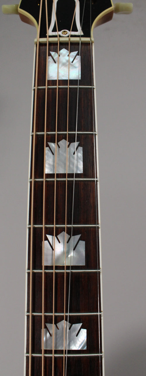 A close-up of the dark rosewood fretboard, showing four mother-of-pearl crown inlays and the top of the headstock.