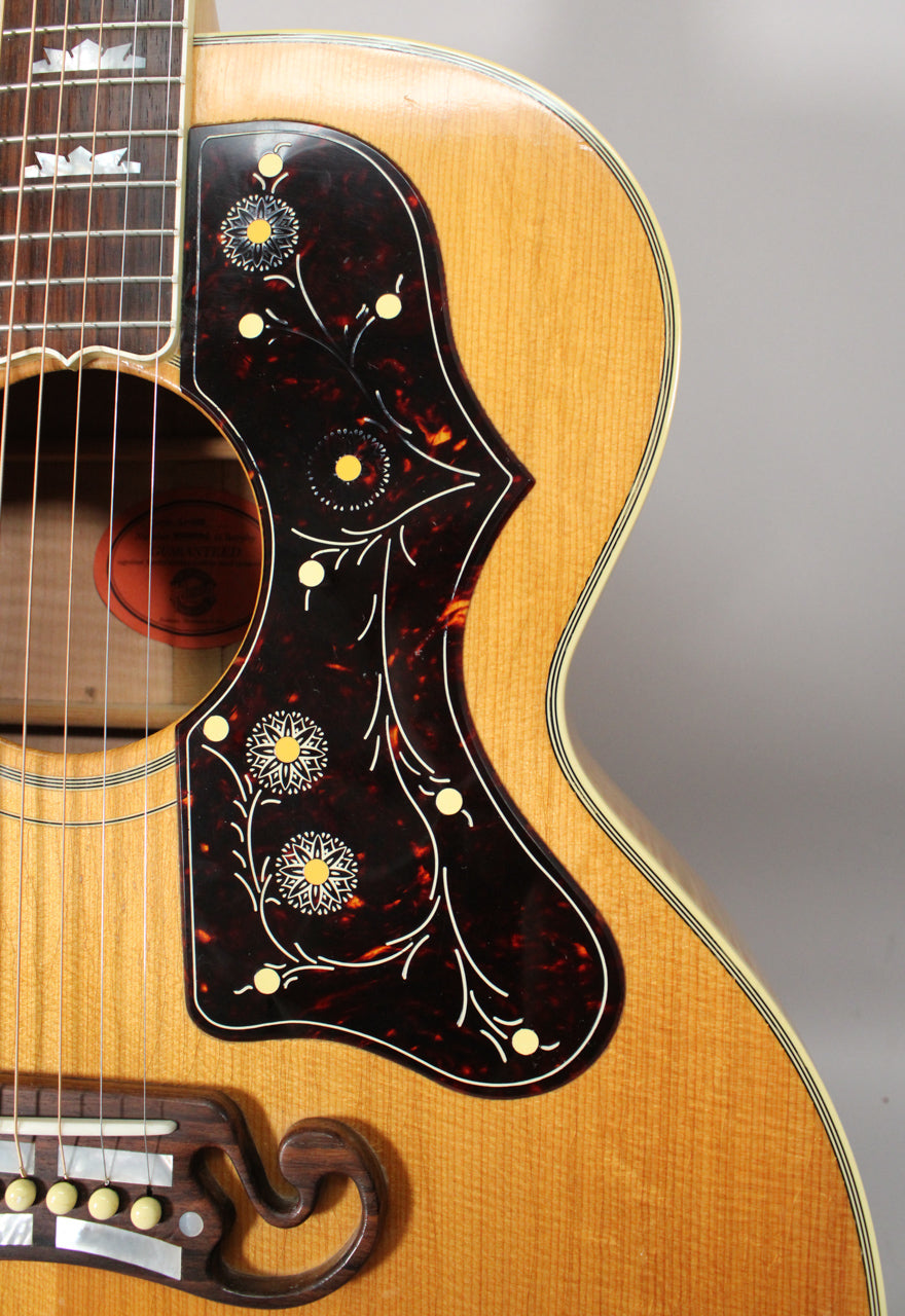 Close-up of the natural finish acoustic guitar's body, showing the ornate tortoiseshell pickguard, bridge, and lower fretboard.